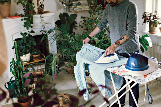 Man ironing his shirt on board in room at home