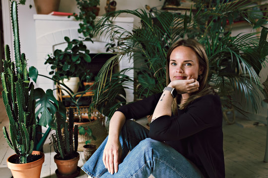 Portrait of woman sitting with hand on chin against plants at home