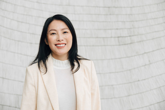 Portrait of smiling businesswoman in blazer standing against wall at office