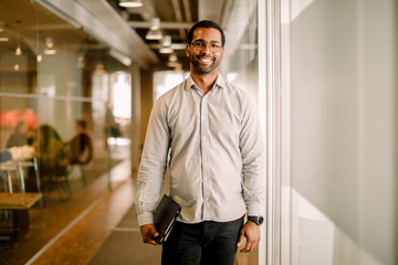 Portrait of smiling businessman standing in office corridor