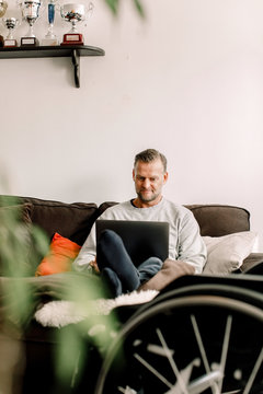 Disabled mature man using laptop while sitting on sofa at home