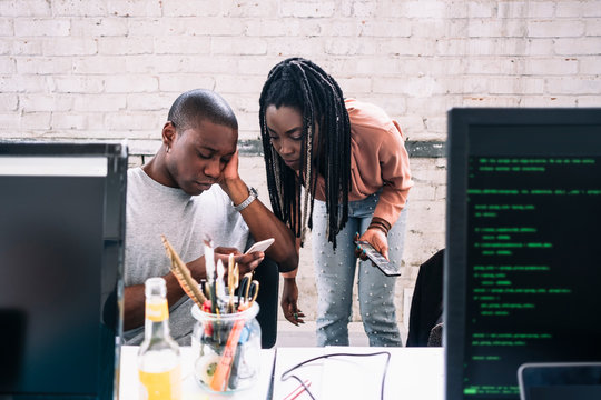 Young businesswoman looking at businessman using smart phone in creative office