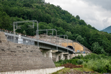 Fototapeta na wymiar A modern railway bridge leads to a tunnel in the mountain.