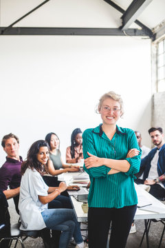 Portrait of smiling female computer hacker with arms crossed standing against team at workplace