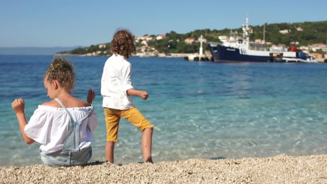 Rear view, schoolchildren curly boy and girl playing with each other on the shores of the Mediterranean. Adriatic, Croatia, Dolmatia region. Travel concept