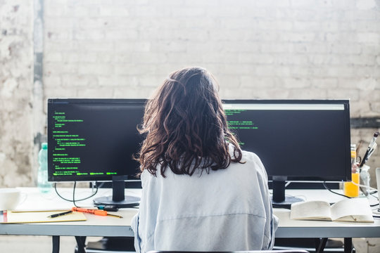 Rear view of female computer hacker coding at desk in creative office