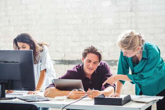 Male computer programmer connecting cable while discussing with female coworker at desk in office