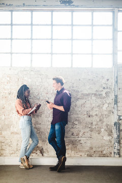 Full length side view of young IT professionals talking while standing by weathered wall in office