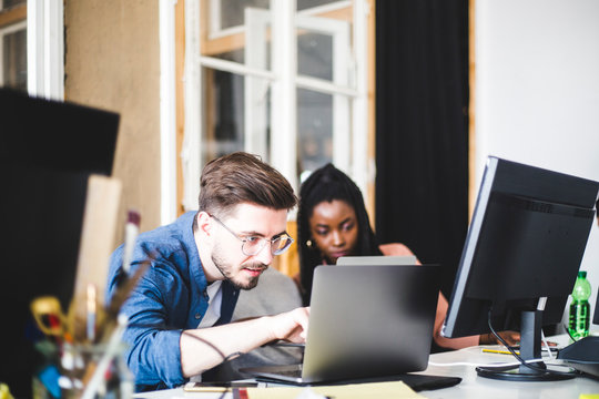 Young computer expert coding in laptop while working with female colleague at workplace