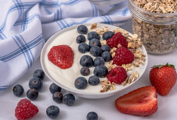 White yogurt in bowl with oatmeal and strawberries, blueberries and raspberries on the top.