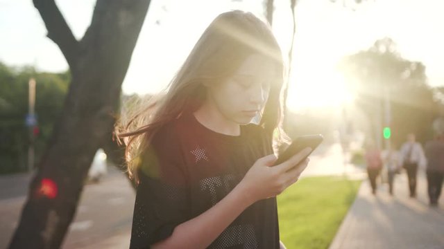 Funny happy teenager girl use phone at sunset street young beautiful casual cell communication device lifestyle outdoors caucasian pretty technology watch internet close up portrait slow motion