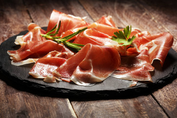 Italian prosciutto crudo or jamon with rosemary. Raw ham on wooden board