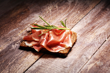 Italian prosciutto crudo or jamon with rosemary. Raw ham on wooden board