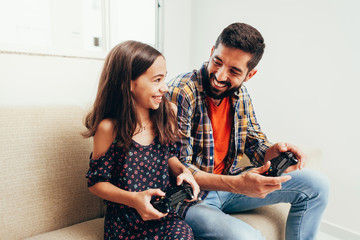 Smiling father and daughter playing video game at home
