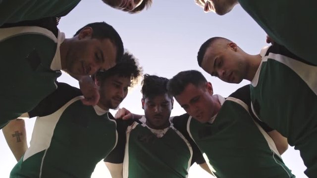 Low angle view of rugby players in circle discussing their tactics. Team of rugby player in huddle between the match.