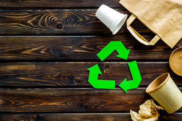 Green recycling sign with waste materials, cups, paper bag for ecology save concept wooden background top view copyspace
