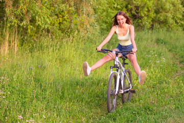 Fototapeta na wymiar Happy pretty young woman riding on a bicycle in a summer park