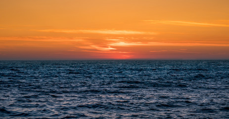 Dusk over Atlantic ocean in Portugal. Bright orange sky and dark blue ocean with horizon center frame