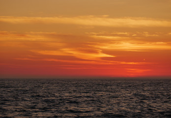 Obraz premium Orange gradient sky at dusk over ocean, just after sunset with dark waves below.