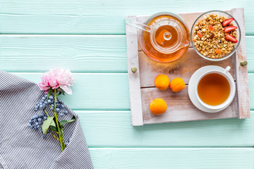 Breakfast in bed with granola, tea and fruit on tray on mint green wooden background top view