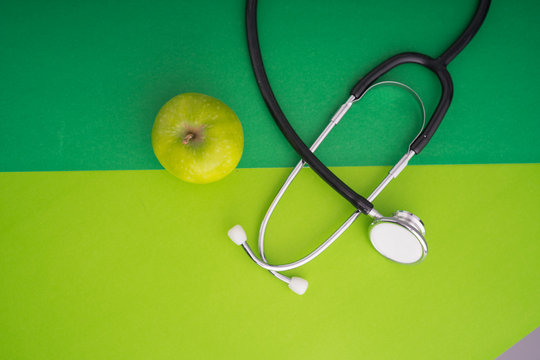 A green apple with stethoscope on green color paper background