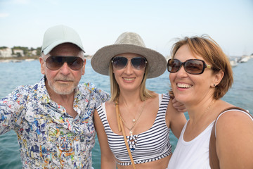 Portrait of two happy women and an older man over seaside promenade taking selfie