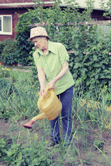 Portrait of elderly woman in a hat with a watering can is watering the beds in her garden.