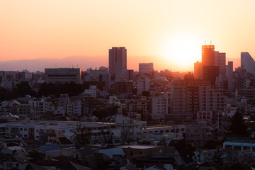 Tokyo, Japan Shinjuku cityscape at sunset with silhouette view of apartment buildings and golden sunlight sun and mountains in background