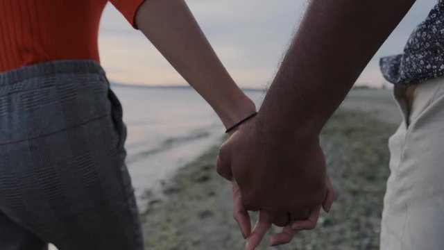 Closeup of young couple holding hands while walking on seashore