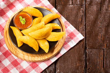 Colombian empanada with spicy sauce on wooden background. Text space