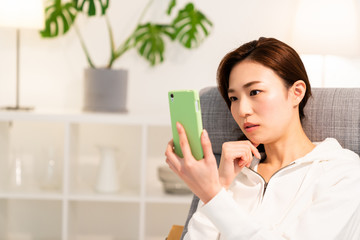 部屋でスマホを見る女性　考える