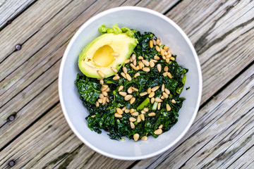 Flat top above view of kale green vegan vegetarian salad on wooden picnic table with pine nuts and avocado half in bowl