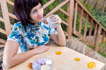 Woman with black asian hair happy smiling sitting at table holding matcha green tea cup outside in backyard garden and daifuku mochi