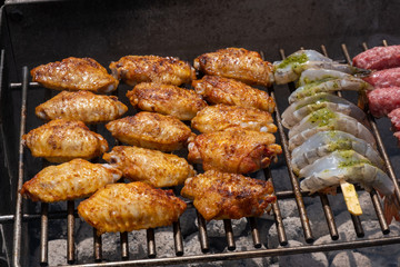 Mixed assortment of marinated meat, chicken, and prawns grilling on hot coals on a BBQ