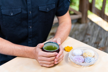 Man sitting at table holding green tea cup outside in backyard garden with Japanese daifuku mochi food