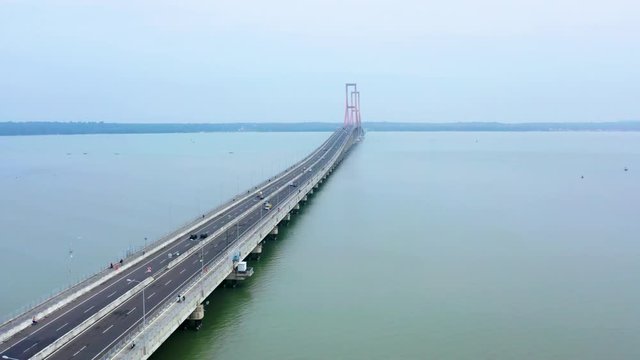 Aerial view of fast traffic over Suramadu bridge on misty morning at Madura strait, East Java, Indonesia. Shot in 4k resolution from a drone flying forwards