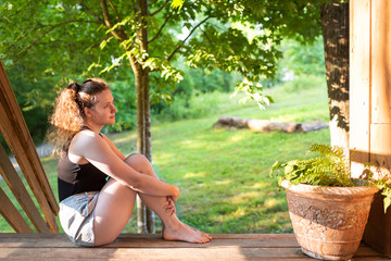 Spring house porch with happy woman sitting on steps of house in front or back yard morning wooden cabin cottage