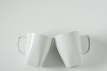 White coffee mugs on white background clinking in cheers with empty copy space
