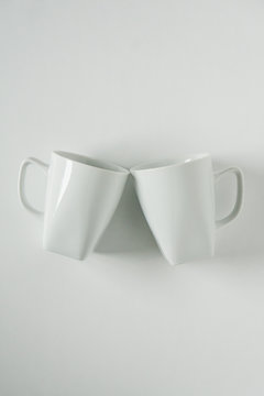 White Coffee Mugs On White Background Clinking In Cheers With Empty Copy Space