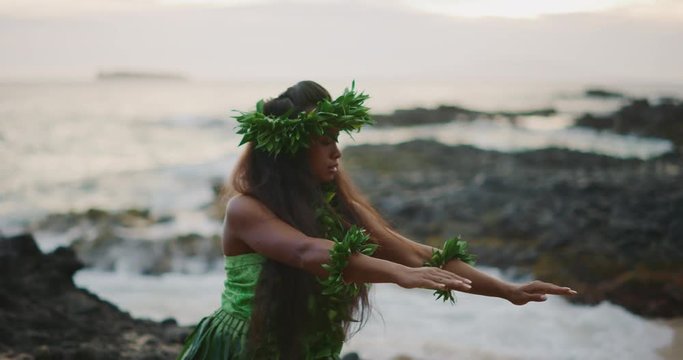Traditional Hawaiian hula dancing at sunset in slow motion, woman performing Hawaiian hula with haku leis and ti leaf skirt