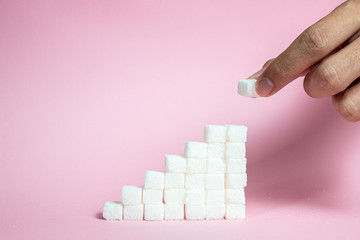 Stack the sugar cubes from ascending to pink background - the concept of high blood sugar risk.