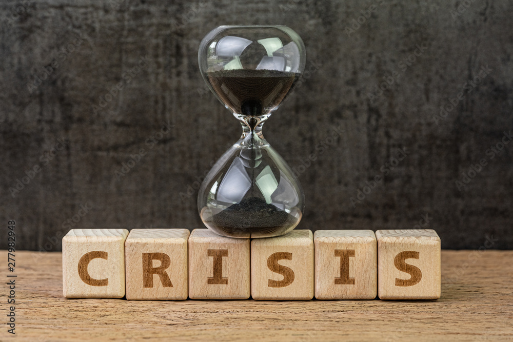 Poster Financial crisis, investment or economic bubble burst countdown concept, sandglass or hourglass on wooden cube block with alphabet building the word Crisis on wood table with dark black background