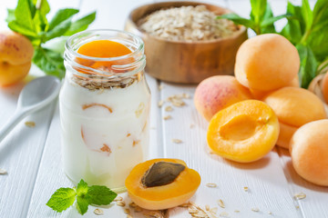 Oatmeal milkshake, smoothie or yogurt with fresh apricot on a white wooden table.