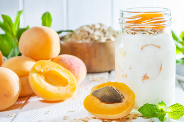 Oatmeal milkshake, smoothie or yogurt with fresh apricot on a white wooden background.
