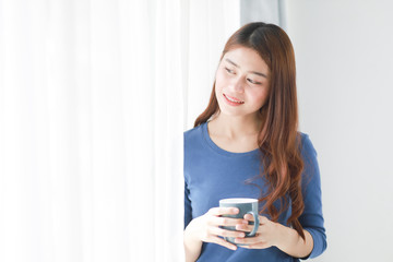 Fototapeta premium Asian woman drinking coffee in living room near the window with take away cup of coffee latte in winter time