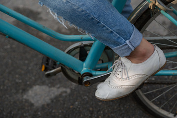 Female wearing jeans and wearing white shoes rides bicycle
