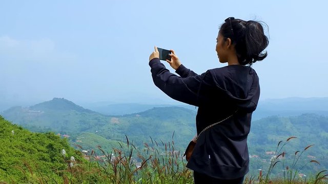 Young woman taking picture with her mobile phone at the peak on misty morning. Shot in 4k resolution