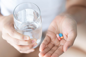 Closeup woman hand holding pills and glass of water, health care and medical concept, selective focus