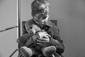 Homeless little boy with teddy bear sitting indoors