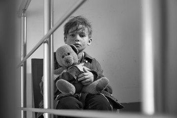 Homeless little boy with teddy bear sitting indoors